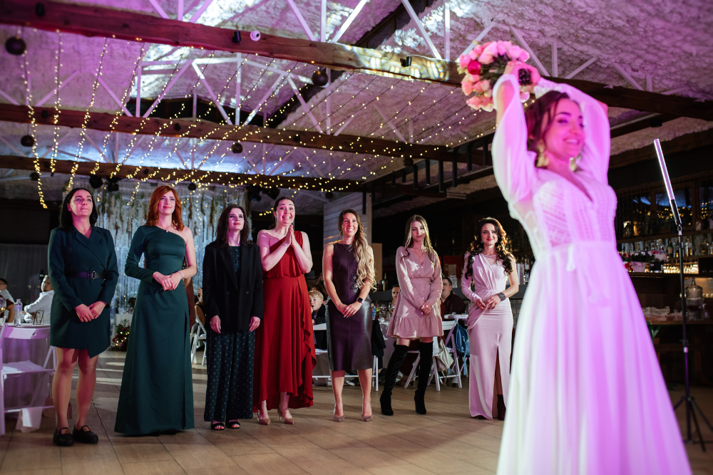 Bride tossing her bouquet at an indoor wedding reception venue as guests cheer.