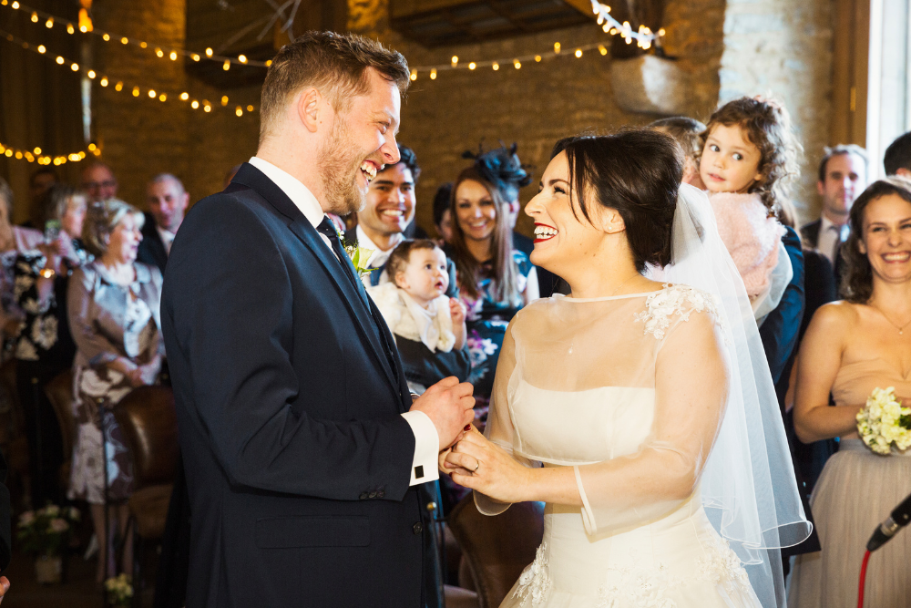 Bride and groom exchanging vows at an indoor wedding reception venue surrounded by family and friends.